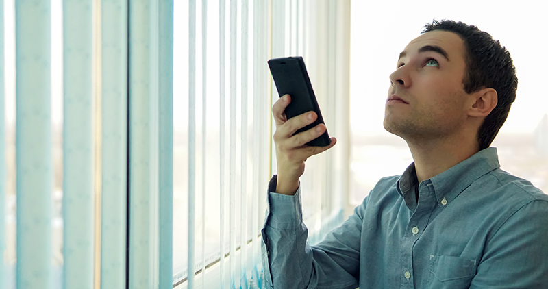 A businessman holds up a remote controller in his hand and looks up.